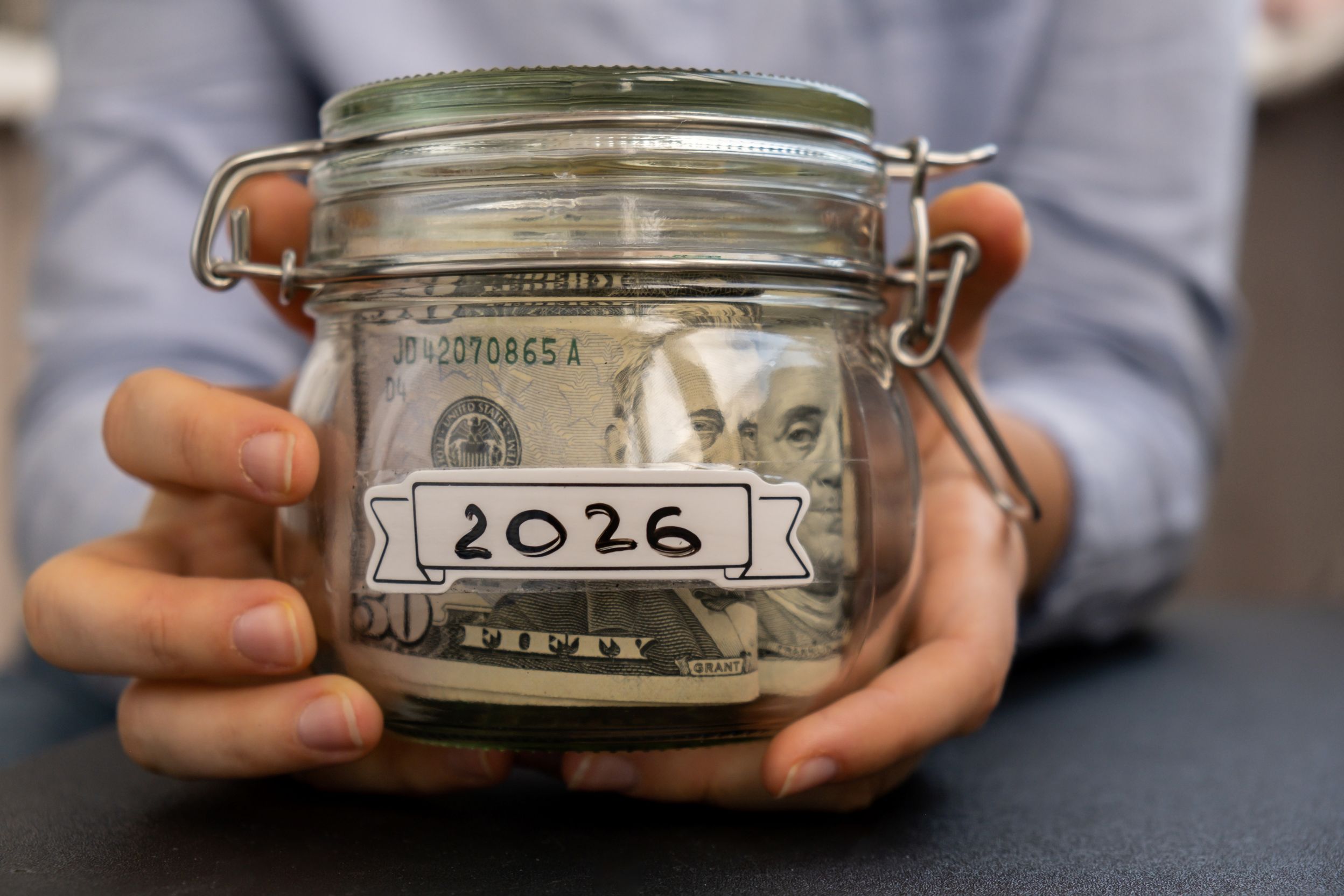 Closeup of adult holding a jar of cash with a label that says 2026.